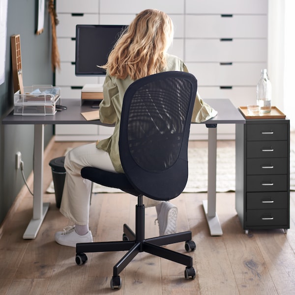 A woman with long blonde hair sitting on an IKEA FLINTAN office chair in front of a black desk.