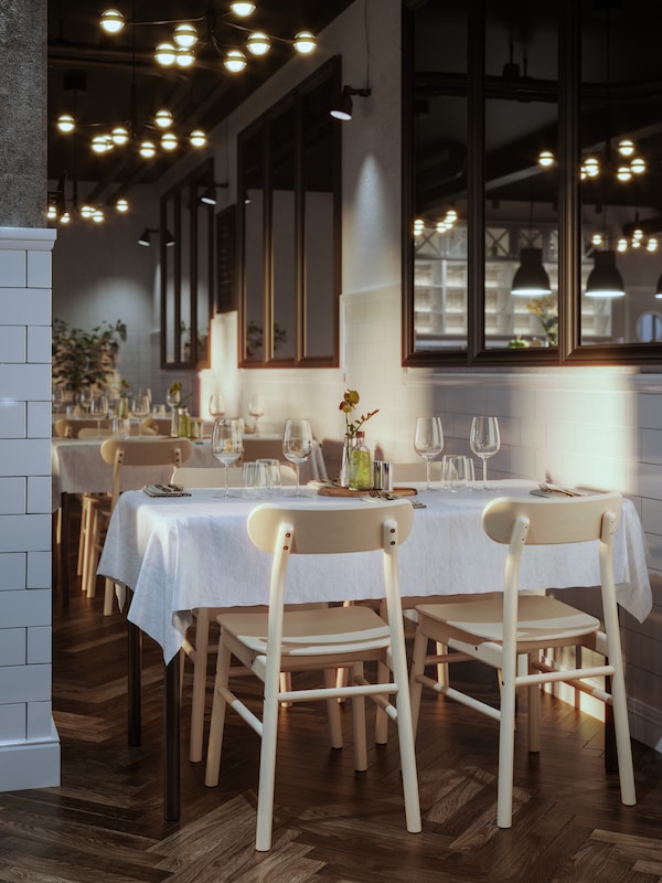 TOMMARYD tables set for dining with white table cloths, STORSINT wine glasses and flowers in a parqueted spacious restaurant.