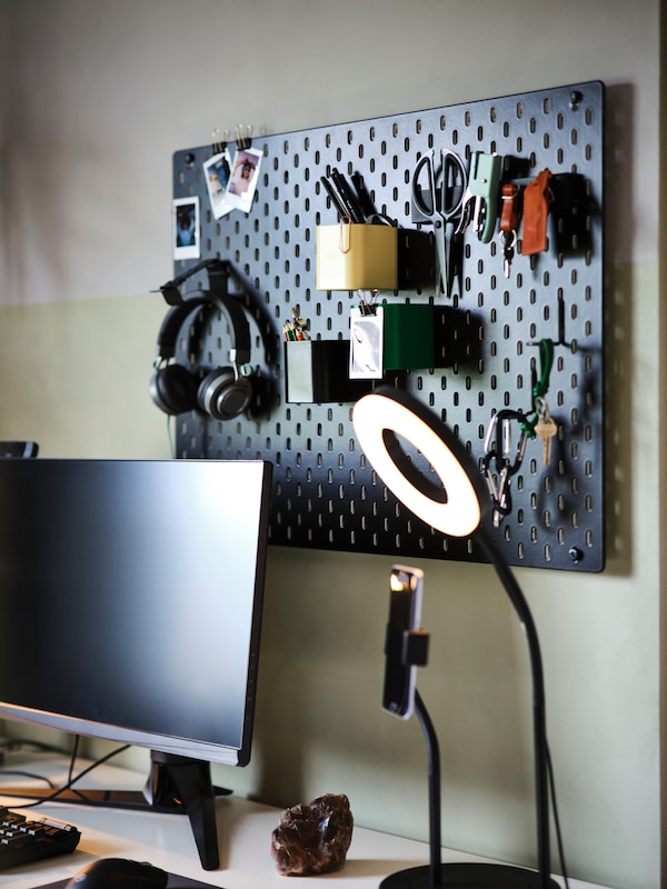 An IKEA SKÅDIS black pegboard on a beige wall with office and gaming accessories attached.