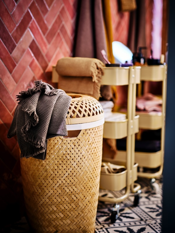 SALUDING bamboo laundry basket against a red tilled wall and yellow RASKOG trolleys