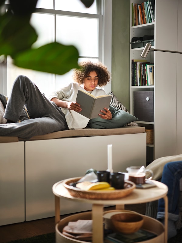 A boy lies on a SMÅSTAD storage box reading a book