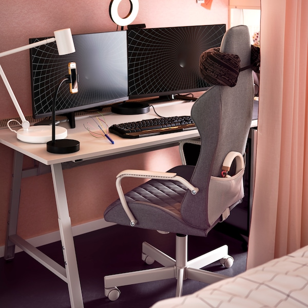 An IKEA UTESPERLARE gaming desk in white, a keyboard and computer screens on top, and a grey gaming chair.