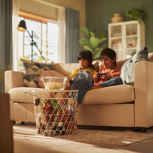 Two children playing video games on a beige IKEA VIMLE sofa in a luminous living room, a white coffee table in front.