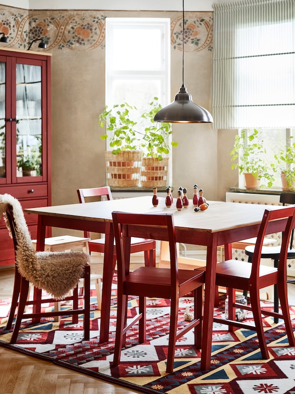 A sunny living room with an IKEA PINNTORP dining table in oak and red, matching red dining chairs, a patterned rug underneath