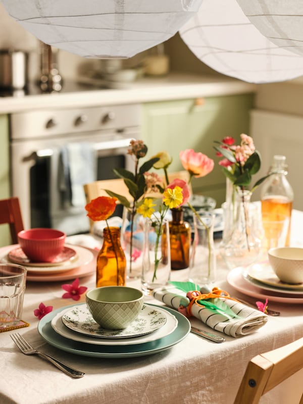 A table with a natural/beige tablecloth and place settings with various dinnerware and KEJSERLIG bowls in mixed colours.