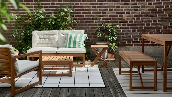 A birdseye view of a balcony decked with RUNNEN acacia wood decking and decorated with NÄMMARÖ acacia table and chairs and plants.