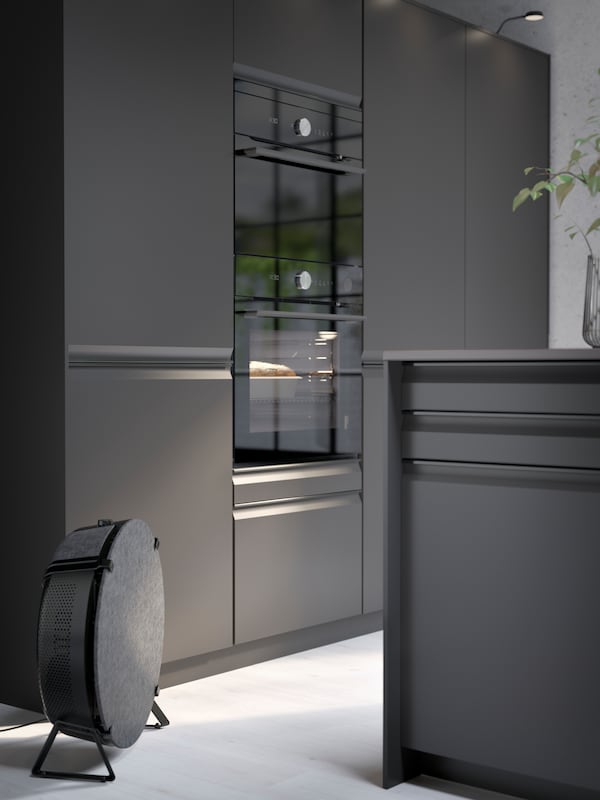 A METOD high cabinet with dark grey modern doors and 2 modern FINSMAKARE ovens.