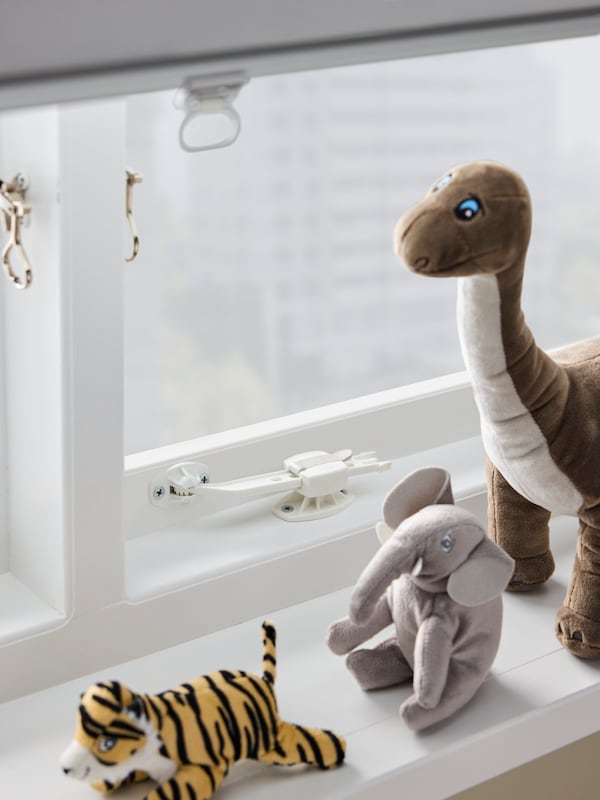 A white UNDVIKA window catch mounted on a window with a white block-out roller blind, plus various soft toys on the sill.