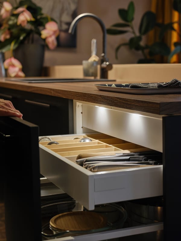 A kitchen drawer with a drawer light turned on and a bamboo cutlery organiser inside.