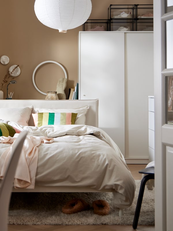 A white KLEPPSTAD bed with ÄNGSLILJA bed linen stands in front of a white KLEPPSTAD wardrobe with sliding doors.