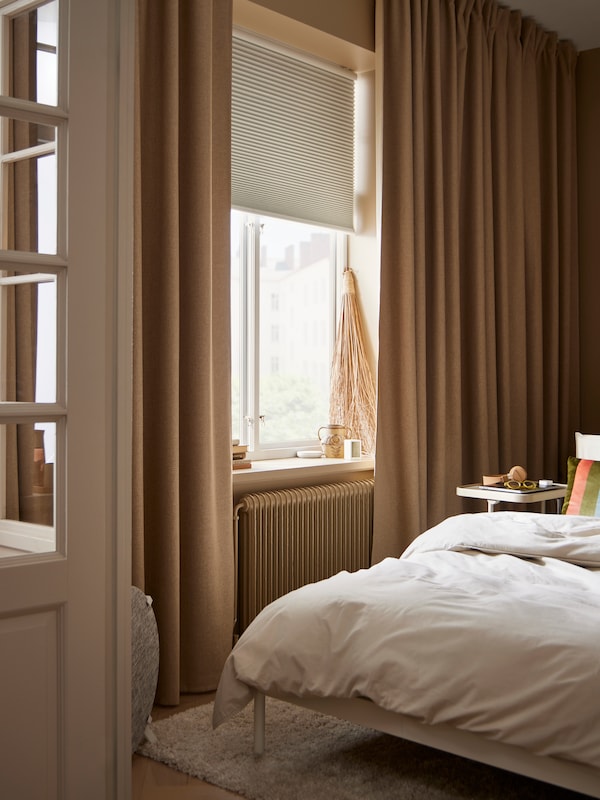 A KLEPPSTAD bed stands in front of a window with a TREDANSEN block-out cellular blind and ANNAKAJSA room darkening curtains.