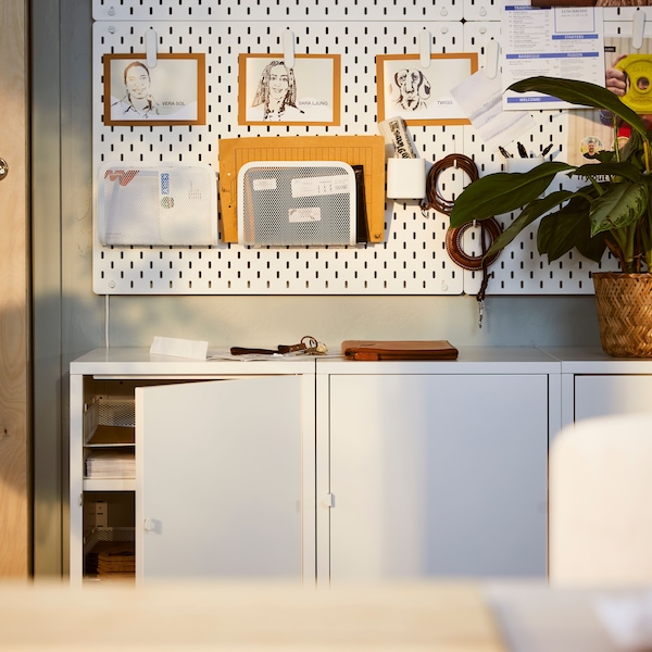 A light office interior a row of white HÄLLAN cabinets with sliding doors beneath a combination of white SKÅDIS pegboards.