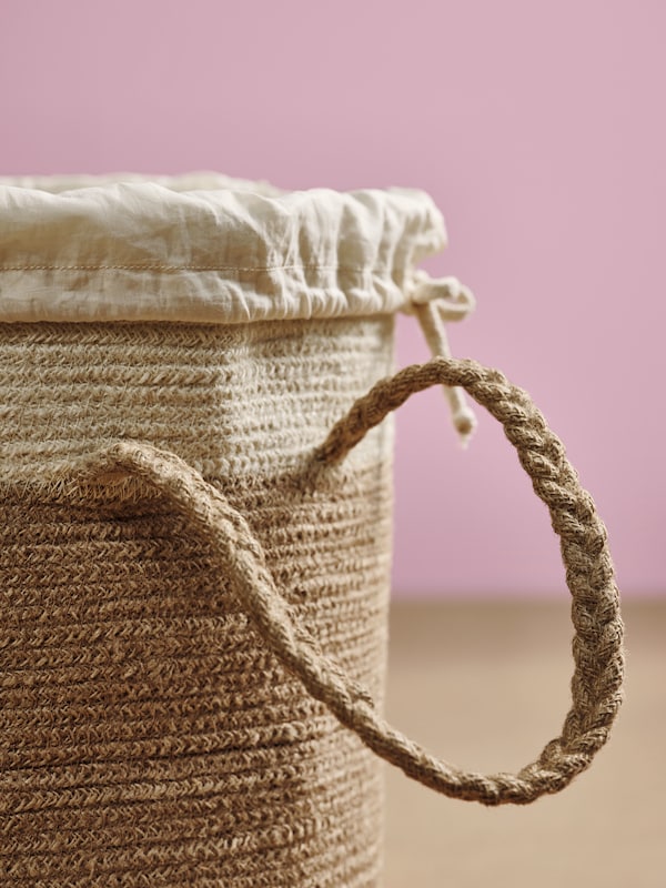 The section of a LJUNGAN jute laundry bag where a braided handle is attached and the cotton lining is folded over the rim.