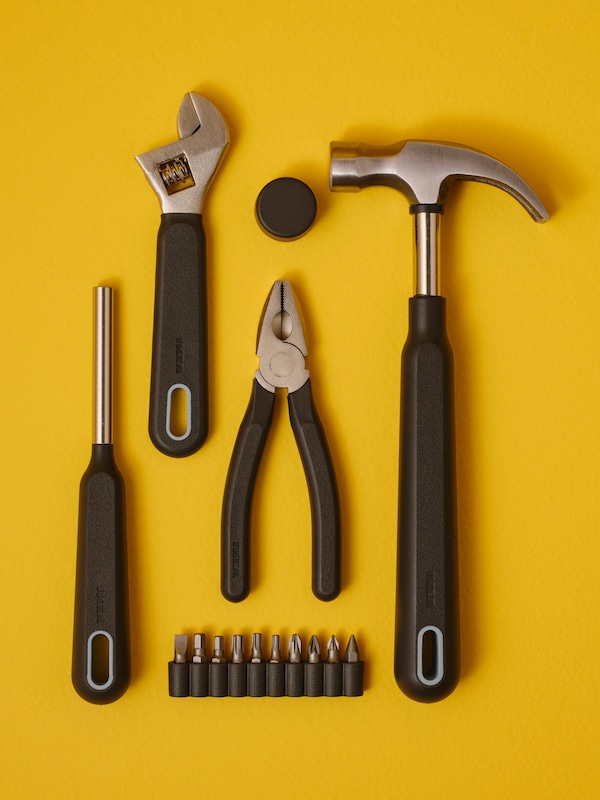 A hammer, a screwdriver, an adjustable wrench and other TRIXIG tools lie neatly arranged on a bright yellow surface.