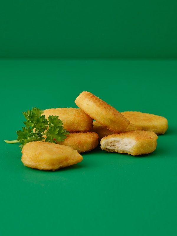 A fried-golden stack of SLAGVERK breaded wheat-based pieces, and a sprig of parsley, arranged on a green surface.