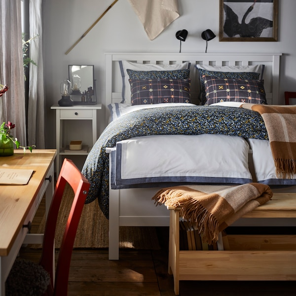 A sundrenched bedroom with a neatly made bed and decorated with a MYRHULL throw and HEMNES and a bedside table.