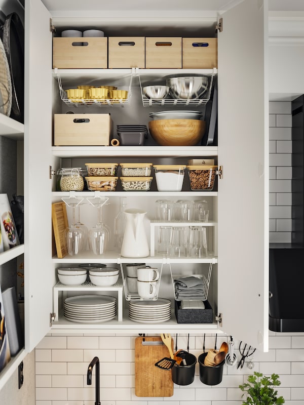 A METOD kitchen wall cabinet open showing white UTRUSTA shelves with containers, plates and glasses.