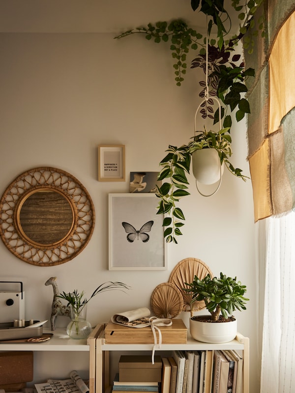 The corner of room with a bohemian style features FEJKA hanging plants, an EKENABBEN open shelving unit and framed art.