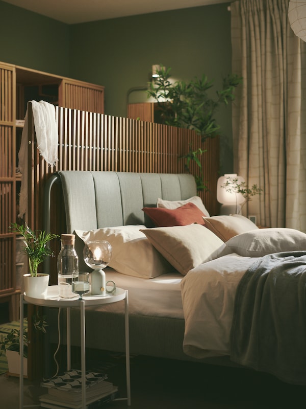 A grey-green TÄLLÅSEN upholstered bed frame with NÄMMARÖ privacy screens behind stands in a serene green bedroom.