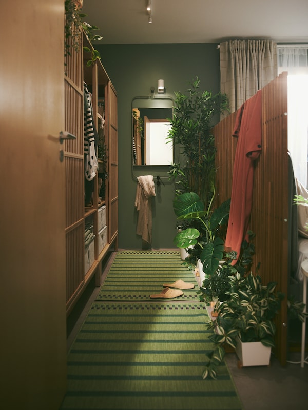 A walk-in closet in a green bedroom is composed of privacy screens, open wardrobes with sliding doors, rugs and plants.