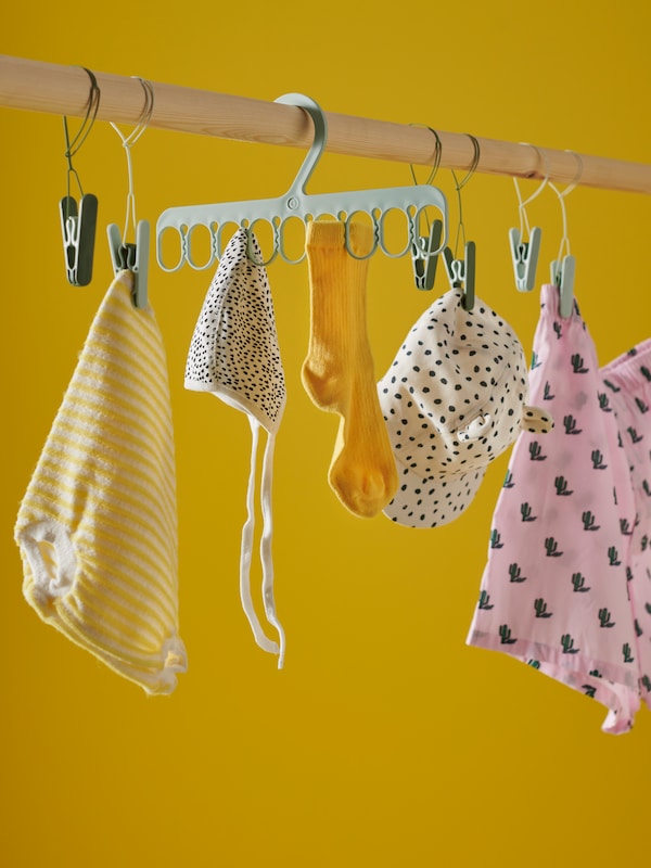 Colourful and patterned baby clothing hang from green SLIBB clothes pegs and SLIBB hanger in a bright yellow space.