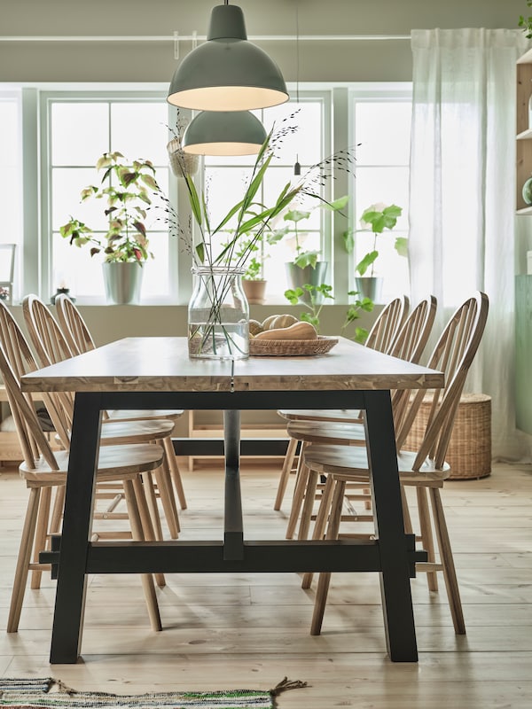 A large IKEA SKOGSTA dining table in acacia wood top and black legs, with acacia dining chairs in a sunny room.