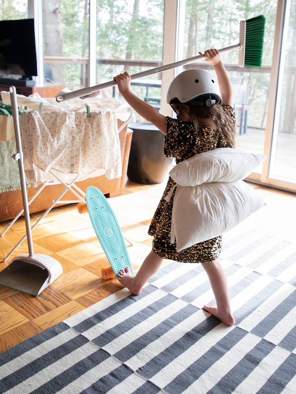 A child in a living room playing with a skateboard and the PEPPRIG dustpan and broom.