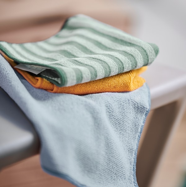 A close-up of a set of three PEPPRIG microfiber cloths in different colours placed on an ironing board.
