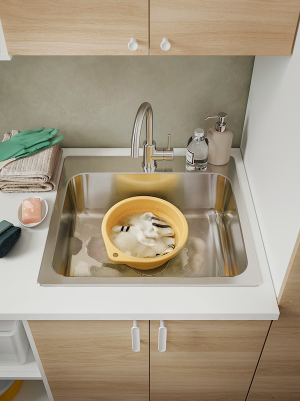 A PEPPRIG wash-tub with some soapy water and socks in it, placed inside a sink.