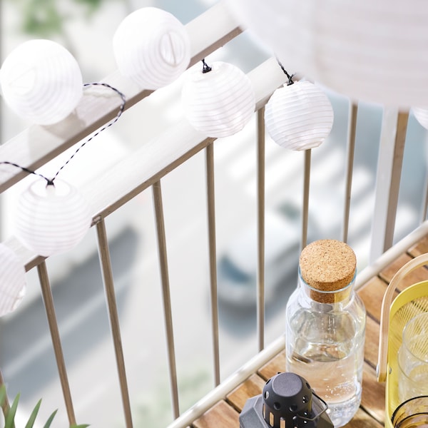 A close-up of a balcony railing with a white SOLVINDEN LED lighting chain with 12 lights around it and beside a table.