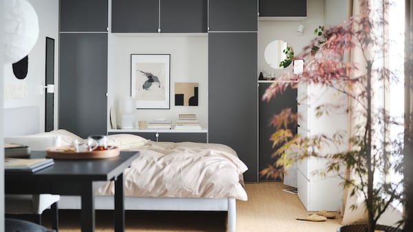 A calm bedroom with a large bed, a wooden desk, a dynamic grey wardrobe and a round lamp hanging from the ceiling.