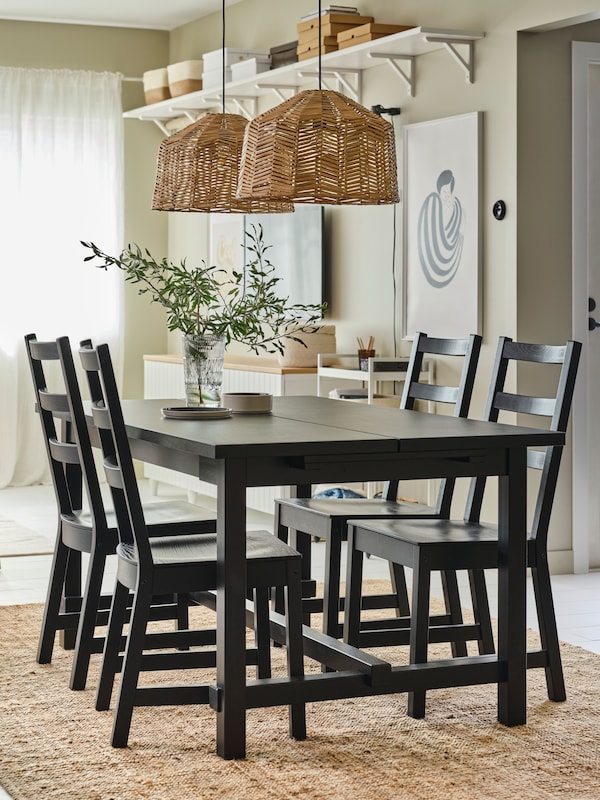 A NORDVIKEN black dining table in a sunny room, with matching black chairs on top of a jute rug.