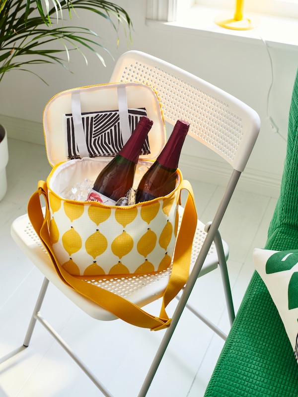 An IKEA NÄBBFISK cooling bag in yellow and white on a white dining chair.