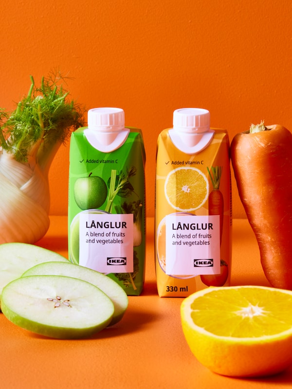 A bright orange space with two LÅNGLUR smoothie packs beside apple slices, half an orange, a carrot, and a fennel.