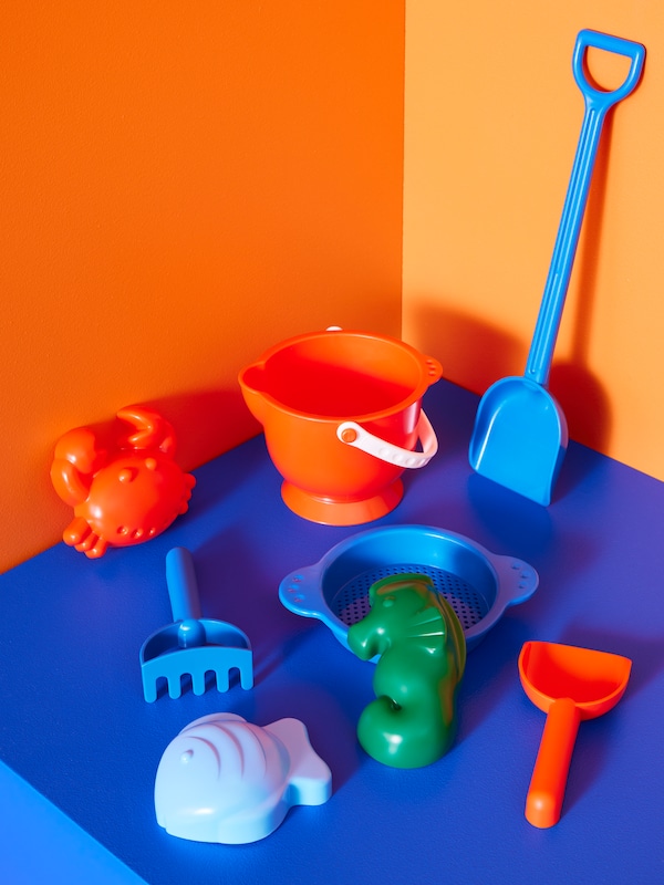 Eight SANDIG plastic sand toys arranged in a space with electric blue floor and orange walls.