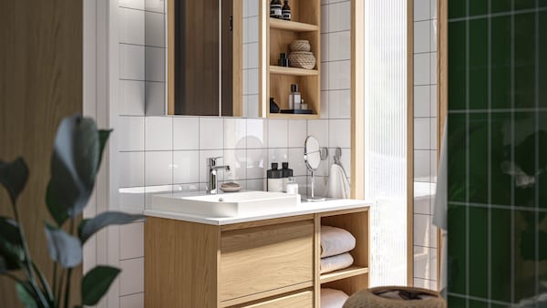 A bathroom with ÄNGSJÖN fronts in oak effect has a washstand with open and closed storage and a mirror cabinet above it.