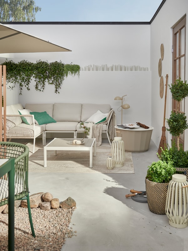 Plants and clusters of SEGERÖN outdoor furniture on a bright, walled gravel-and-stone patio by a single-storey house.