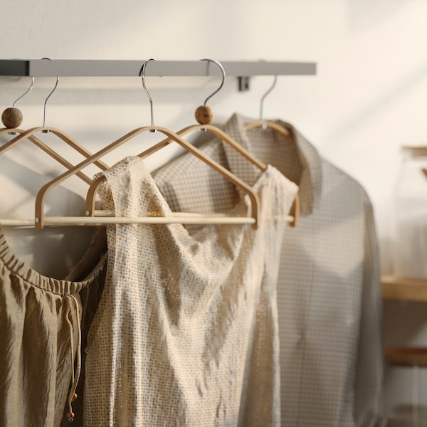 Several blouses and shirts on HÖSVANS bamboo hangers, hanging on a metal wall-mounted rail.