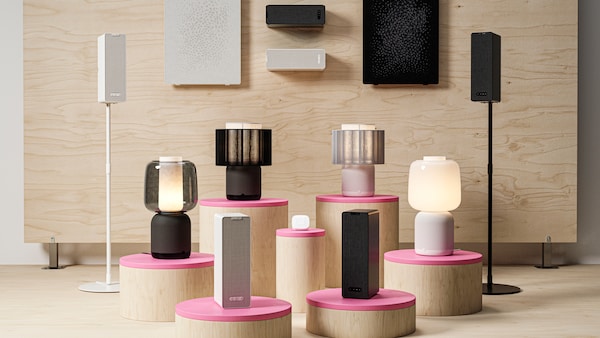 Several SYMFONISK products standing on pedestals, on the floor and hanging on a wooden wall.