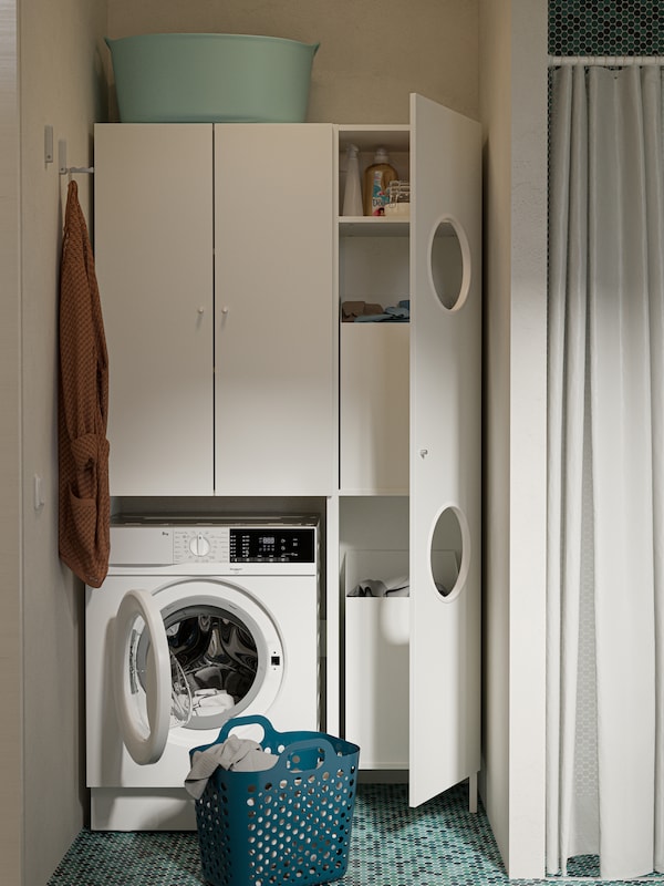 There are white NYSJÖN cabinets next to a shower, a white washing machine and a green basket on a green-tiled floor.