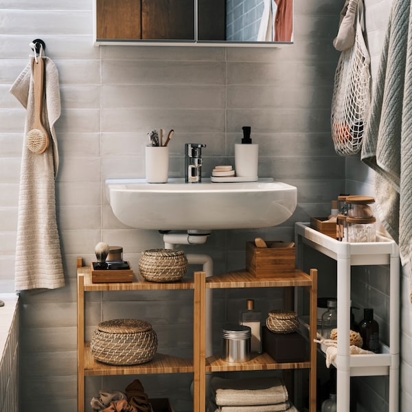 Two bamboo wash-basin/corner shelves under a wash-basin with a mirror cabinet over it, plus a trolley and towels on hooks.