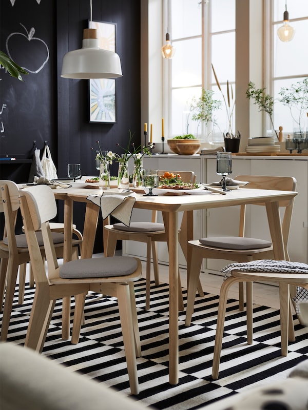 Two LISABO tables in ash veneer and several LISABO chairs in ash are standing on a STOCKHOLM rug in black and off-white.