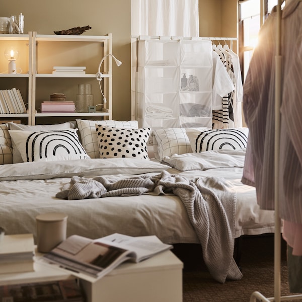 Two LYCKSELE LÖVÅS sofa beds with grey bedding and patterned pillows, plus a white coffee table and white clothes racks.