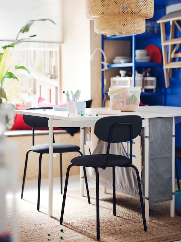 Two ÖSTANÖ chairs are standing next to a white and light grey KALLHÄLL gateleg table with storage in a room with a blue wall.