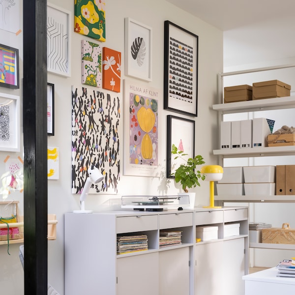 Two SPIKSMED sideboards, one with a yellow BLÅSVERK table lamp on top, stand against a wall decorated with pictures.