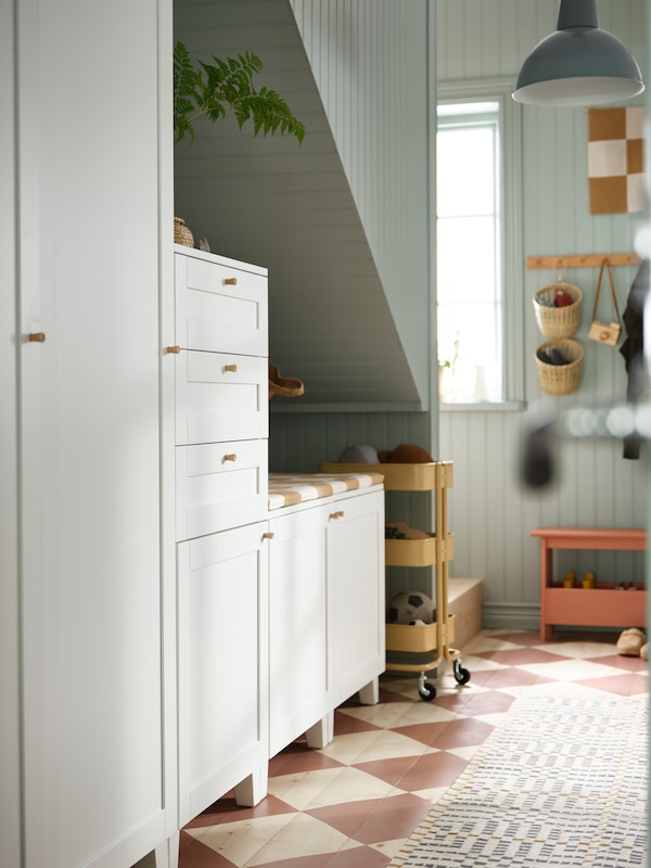 Underneath a stairwell are PLATSA wardrobes and cabinets. On the rust red chequered floor is a VAMDRUP rug.