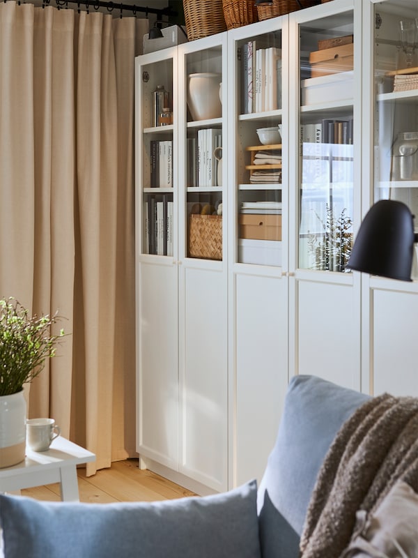 White BILLY bookcases stand against the wall of a traditional-style living room, with books and baskets on its shelves.